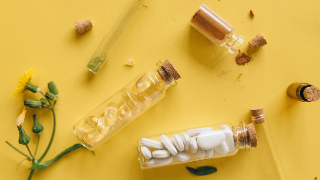 Stock image of pills and herbs in bottles against a sunny yellow backdrop.